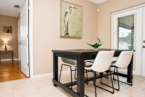 A dining area with a table, chairs, a painting, and a lamp.