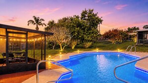 A swimming pool with a glass enclosure, a patio with chairs, and string lights.