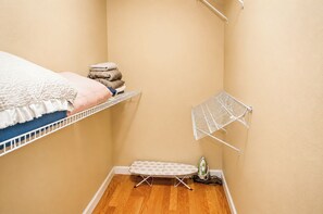 Una stanza piccola con un letto a castello, uno scaffale con asciugamani piegati, uno stendibiancheria, un asse da stiro e un ferro da stiro portatile.