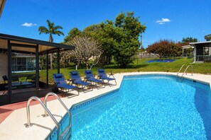 A swimming pool with blue tiles, a covered seating area with chairs, and a fenced garden. - Centrally located 3Br2Ba Pool Home available for LONGER STAYS, Monthly Discounts (Port St. Lucie)