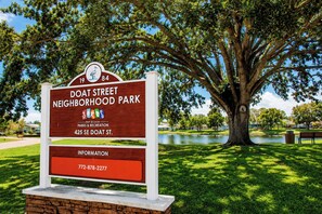 A neighborhood park sign with a large tree and a body of water in the background. - Centrally located 3Br2Ba Pool Home available for LONGER STAYS, Monthly Discounts (Port St. Lucie)