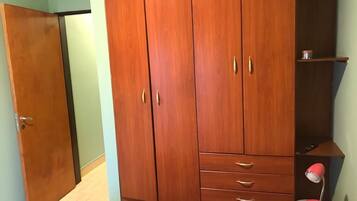 A room with a wooden wardrobe, a small desk, and a pink lamp.