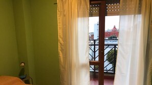 Et værelse med seng, stol og en balkon med gelænder.