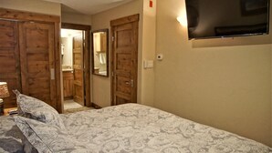 Ein Schlafzimmer mit einem Bett, einem Holzschrank, einem an der Wand befestigten Fernseher und einem Spiegel.
