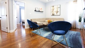 Una sala de estar moderna con un sofá, dos sillas azules, una mesa de centro y un cuadro en la pared.