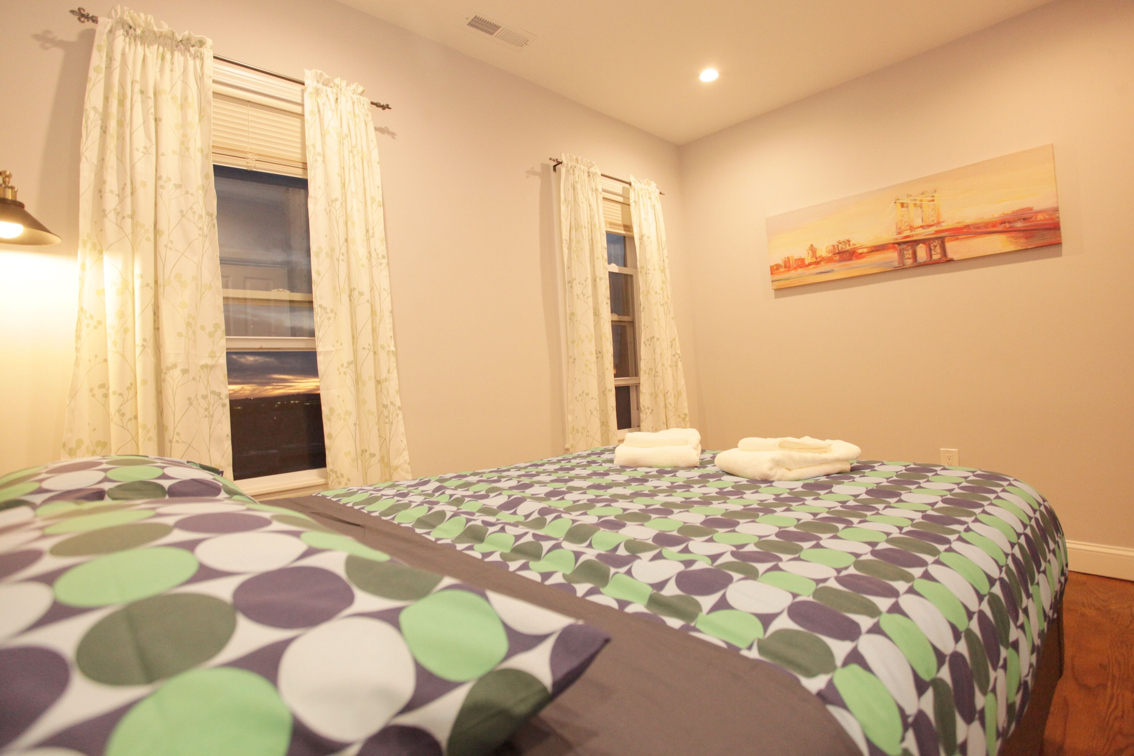 A hotel room with a bed, a window with curtains, a painting on the wall, and a view of the outside.