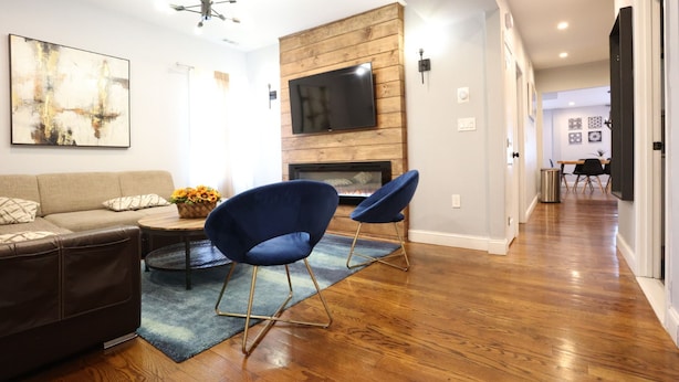 Una sala de estar moderna con un sofá, dos sillones azules, un televisor instalado en una pared de madera y una chimenea.
