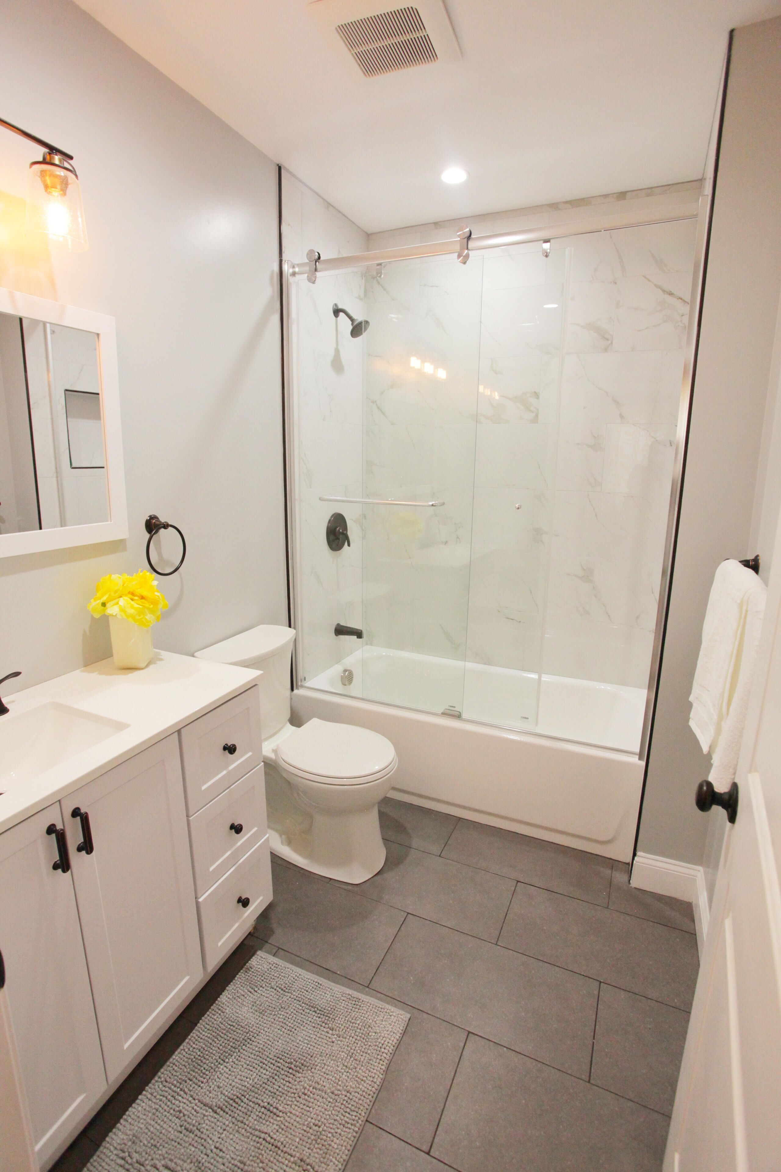 Un baño moderno con ducha envuelta en vidrio, inodoro y lavamanos con espejo y florero.