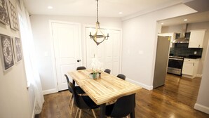 Un comedor con mesa y sillas de madera, una araña y una cocina al fondo.