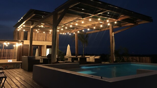 Een overdekt buitenzwembadgedeelte met lichtjes, een houten terras en comfortabele zitplaatsen.