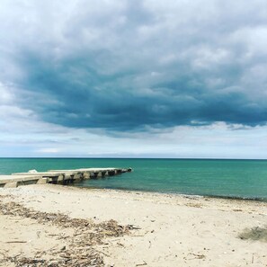 A beach with a concrete breakwater extending into the sea, sandy shore, and overcast sky.