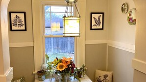 Un coin repas avec une table blanche, un vase de fleurs et une fenêtre donnant sur un jardin.