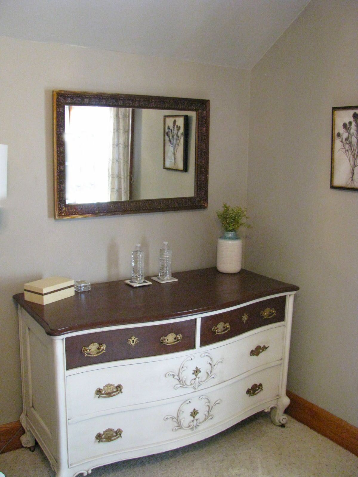 A white dresser with gold handles, a mirror above it, and a framed botanical print on the wall.