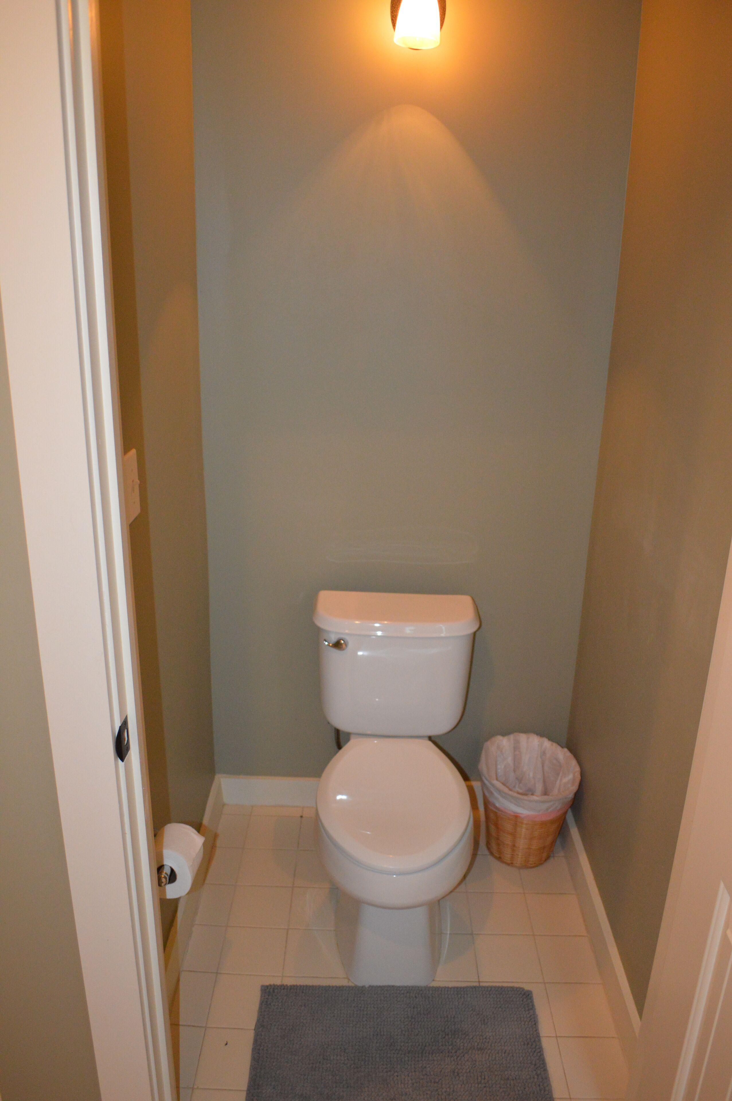 Ein kleines Badezimmer mit Toilette, Mülleimer und Wandleuchte.