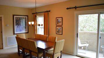 A dining room with a wooden table and six chairs, a chandelier, and two framed pictures on the wall.