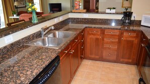 Una cocina con encimeras de granito, armarios de madera, lavavajillas y cafetera.