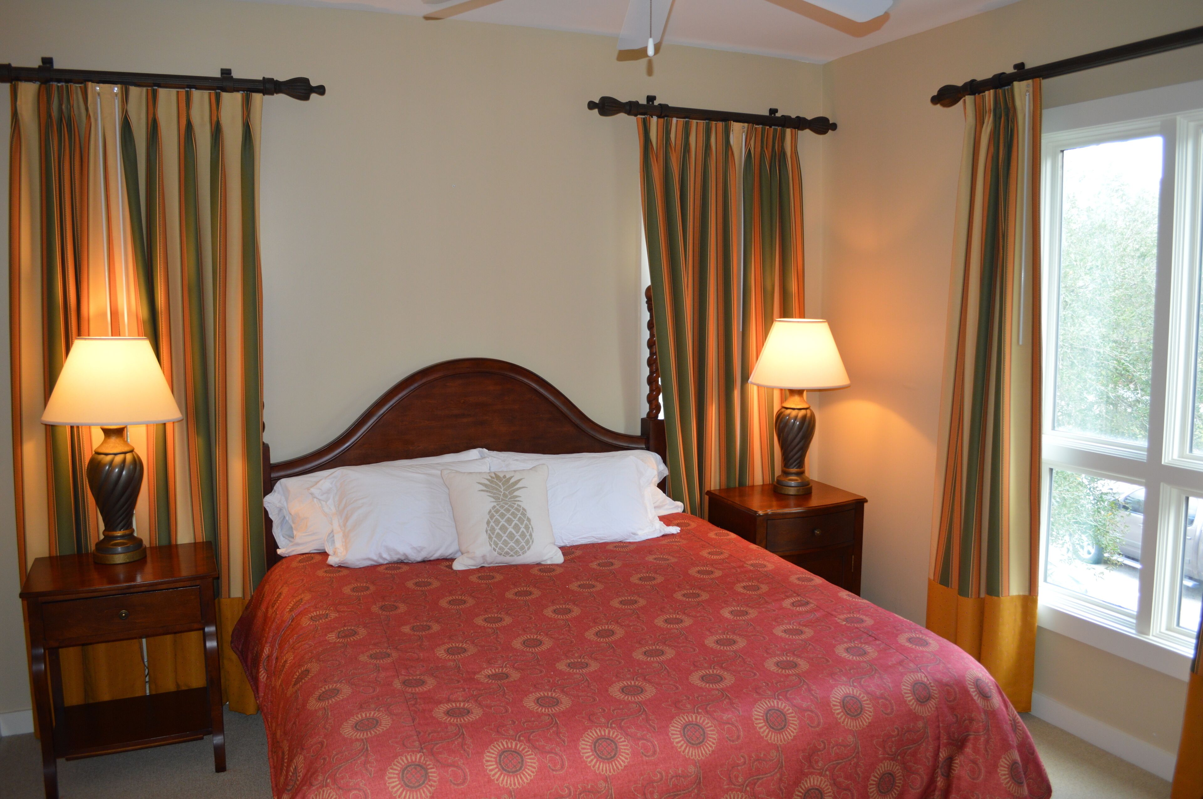 Un lit bien fait, recouvert d’une couvre-lit à motifs, avec deux lampes de chevet et des rideaux de chaque côté.