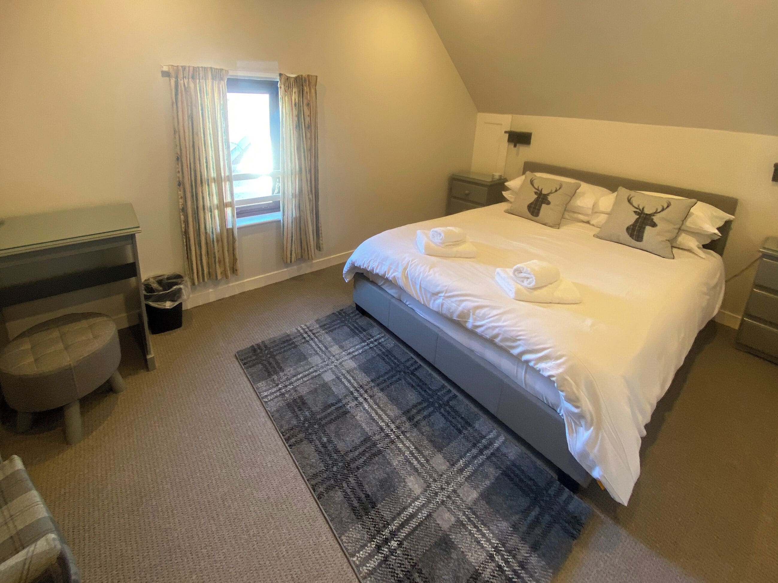 Une chambre d’hôtel avec un lit, des tables de chevet, une chaise, une fenêtre avec des rideaux et un tapis à motifs.