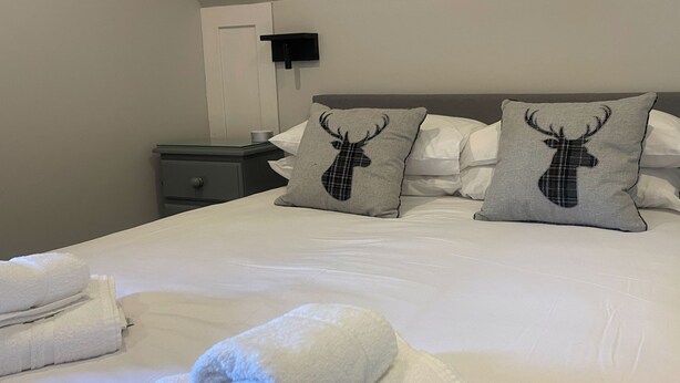 A neatly made bed with white linens and two pillows featuring a deer motif. - 3 bedroom accommodation in Oban (Oban)