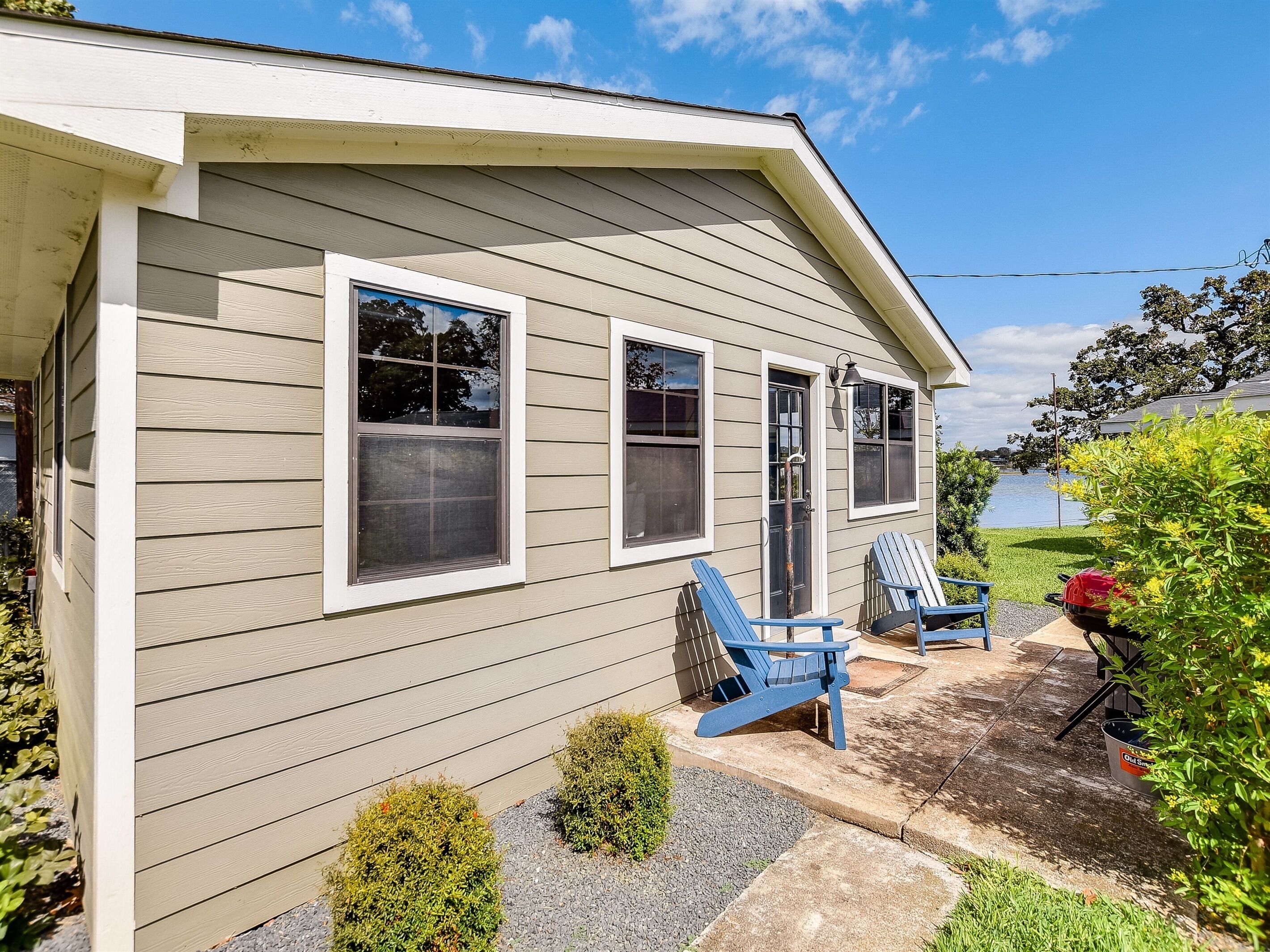 A two-story house with a front porch, two blue Adirondack chairs, and a small garden area.