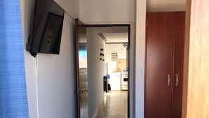 A narrow hallway with a bed on the right, a TV mounted on the wall, and a wooden wardrobe. - Departamento Belgrano 6 (Salta)