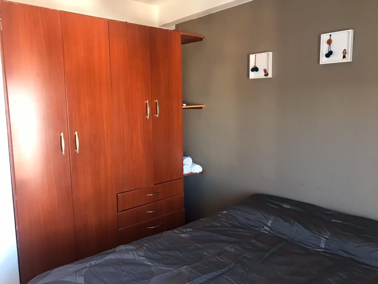 A bedroom with a wooden wardrobe, a bed, and two wall-mounted picture frames.