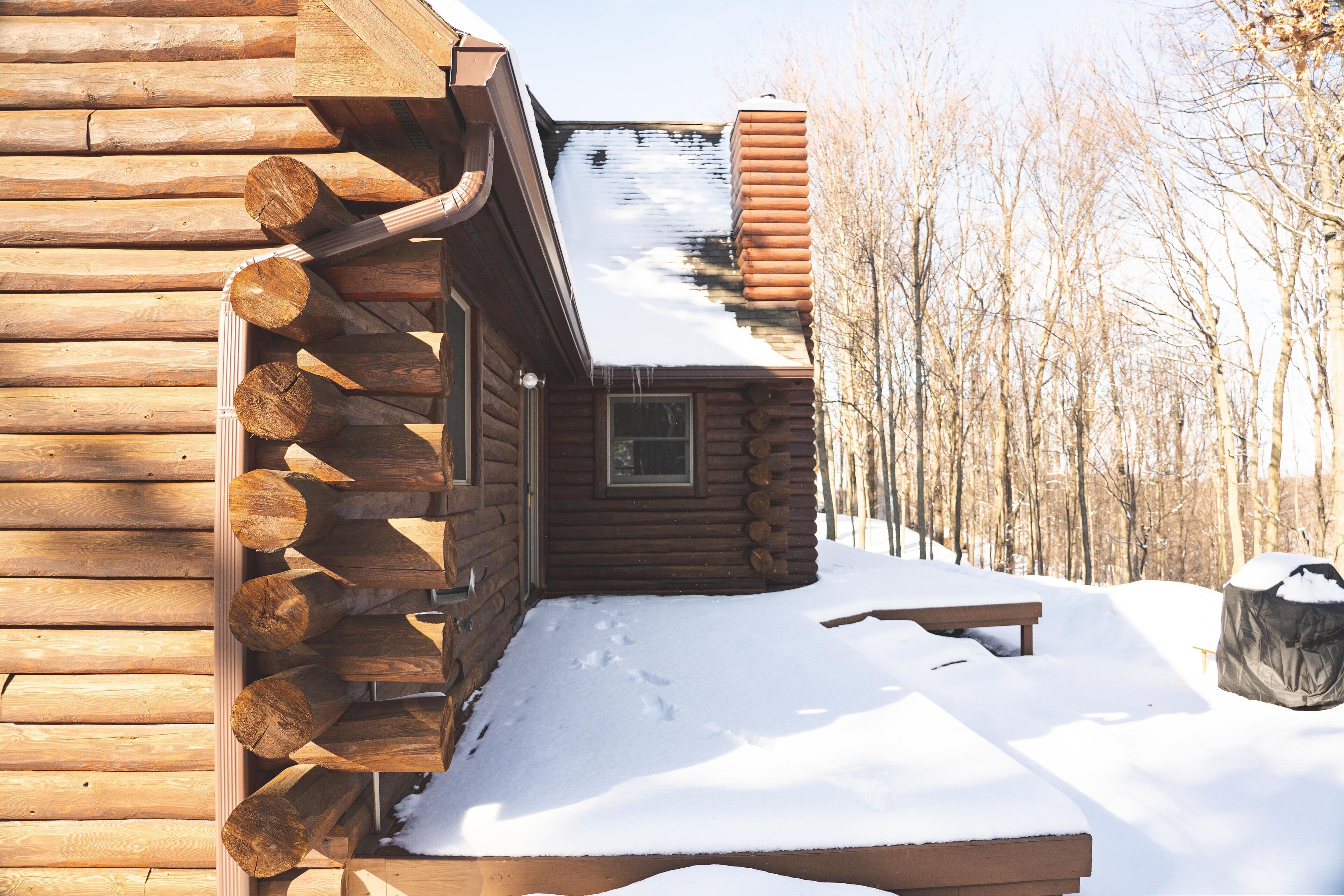 A log cabin with a snow-covered roof and a wooden deck.