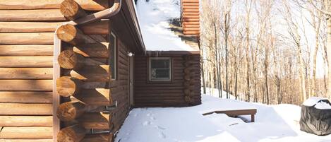A log cabin with a snow-covered roof and a wooden deck.