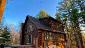 A log cabin with a wooden deck, large windows, and a stone foundation.