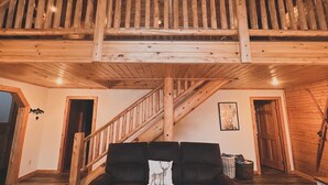 A spacious loft with a high ceiling, wooden beams, a balcony, and a staircase leading to an upper level.