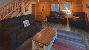 A spacious cabin with a loft bedroom, a cozy living area with a sofa and chairs, and a wooden staircase.