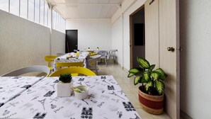 Un coin repas avec des tables préparées pour deux personnes, agrémenté d’une nappe sur le thème de Paris. On y trouve des chaises, une plante en pot et une porte donnant sur une autre pièce.
