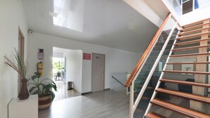 Un hall d’entrée spacieux avec un plancher en bois, un escalier doté de rampes en verre et une plante en pot.