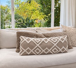 A sofa with patterned cushions and a view of greenery outside.