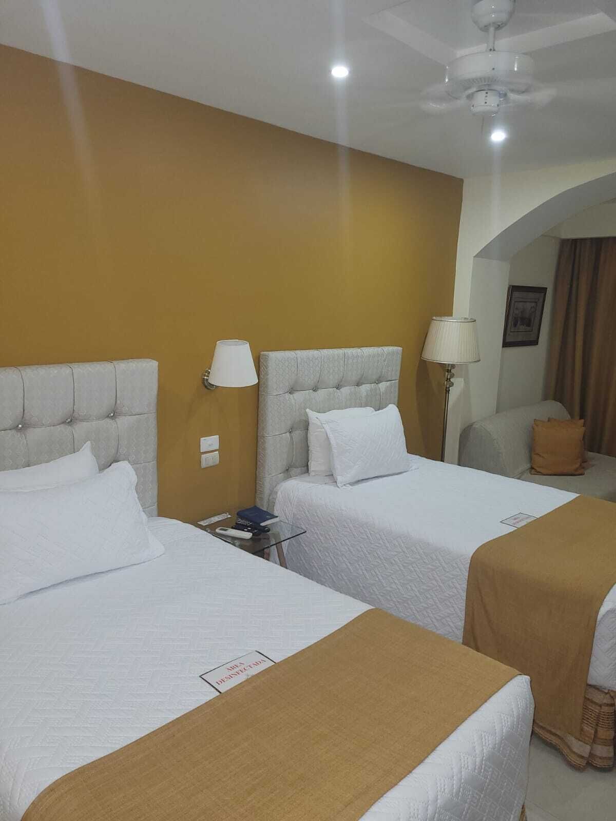 A hotel room with two beds, a ceiling fan, and a small table with a lamp.