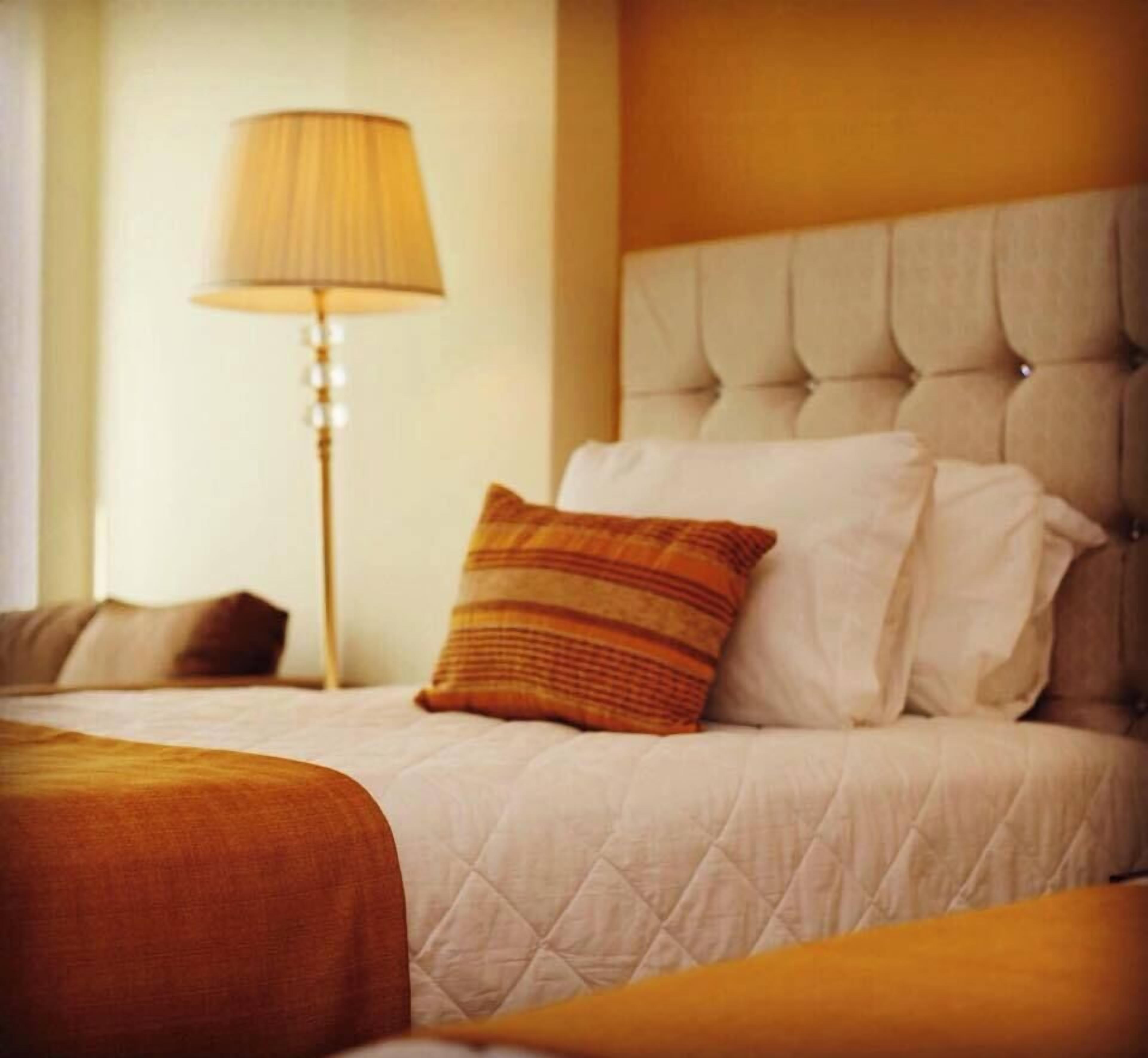 Una habitación de hotel con una cama, una lámpara y un cabecero capitonado.