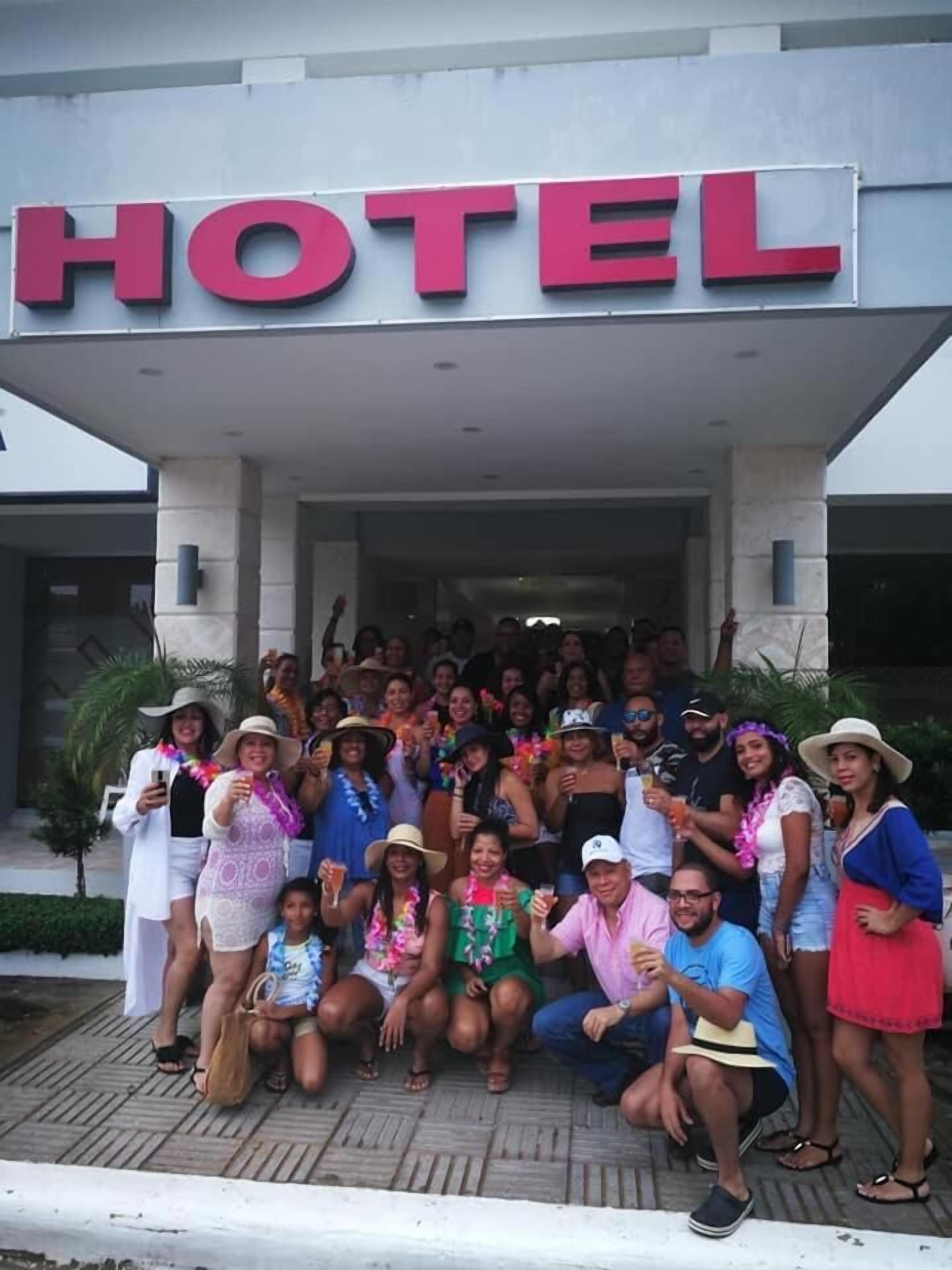 A group of people posing in front of a hotel entrance with a prominent 'HOTEL' sign.