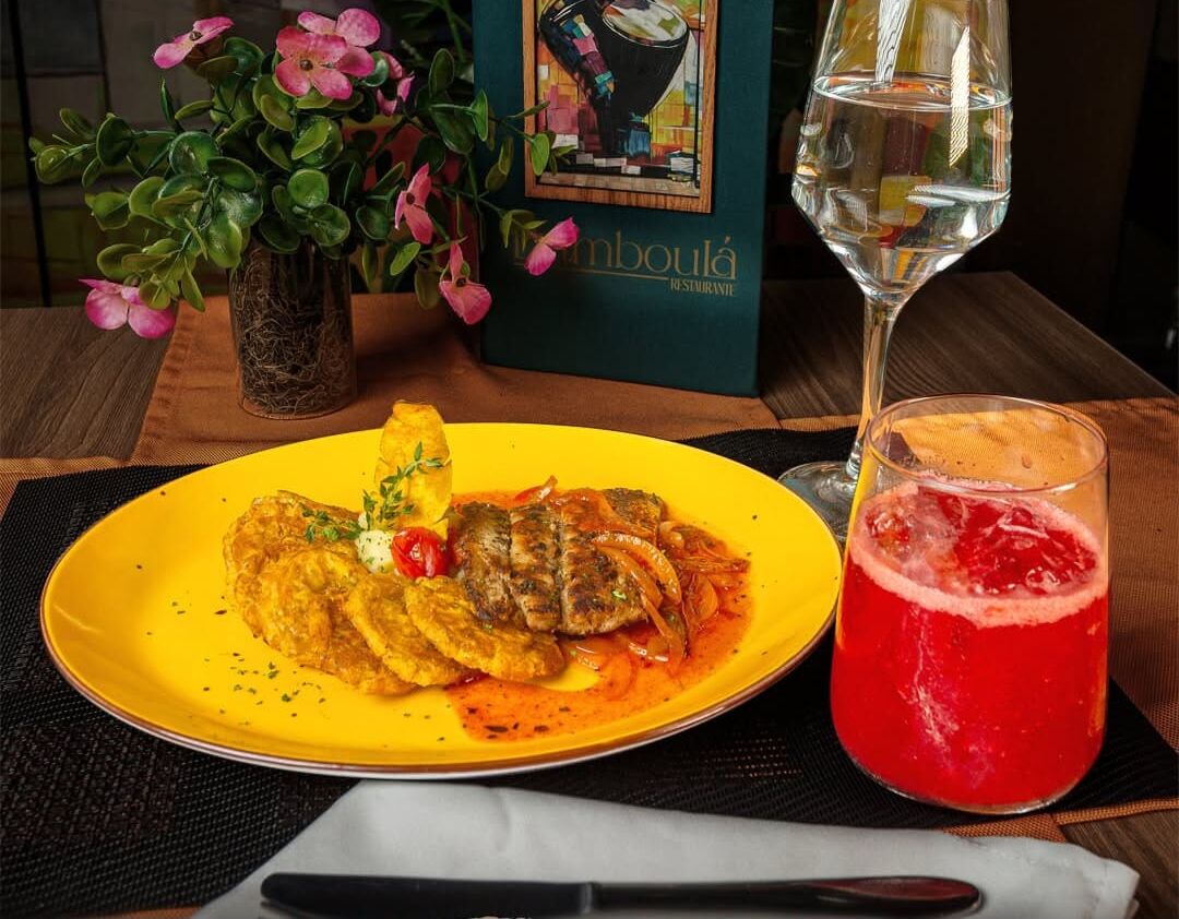 A dining table with a plate of food, a glass of red drink, and a bottle of water.