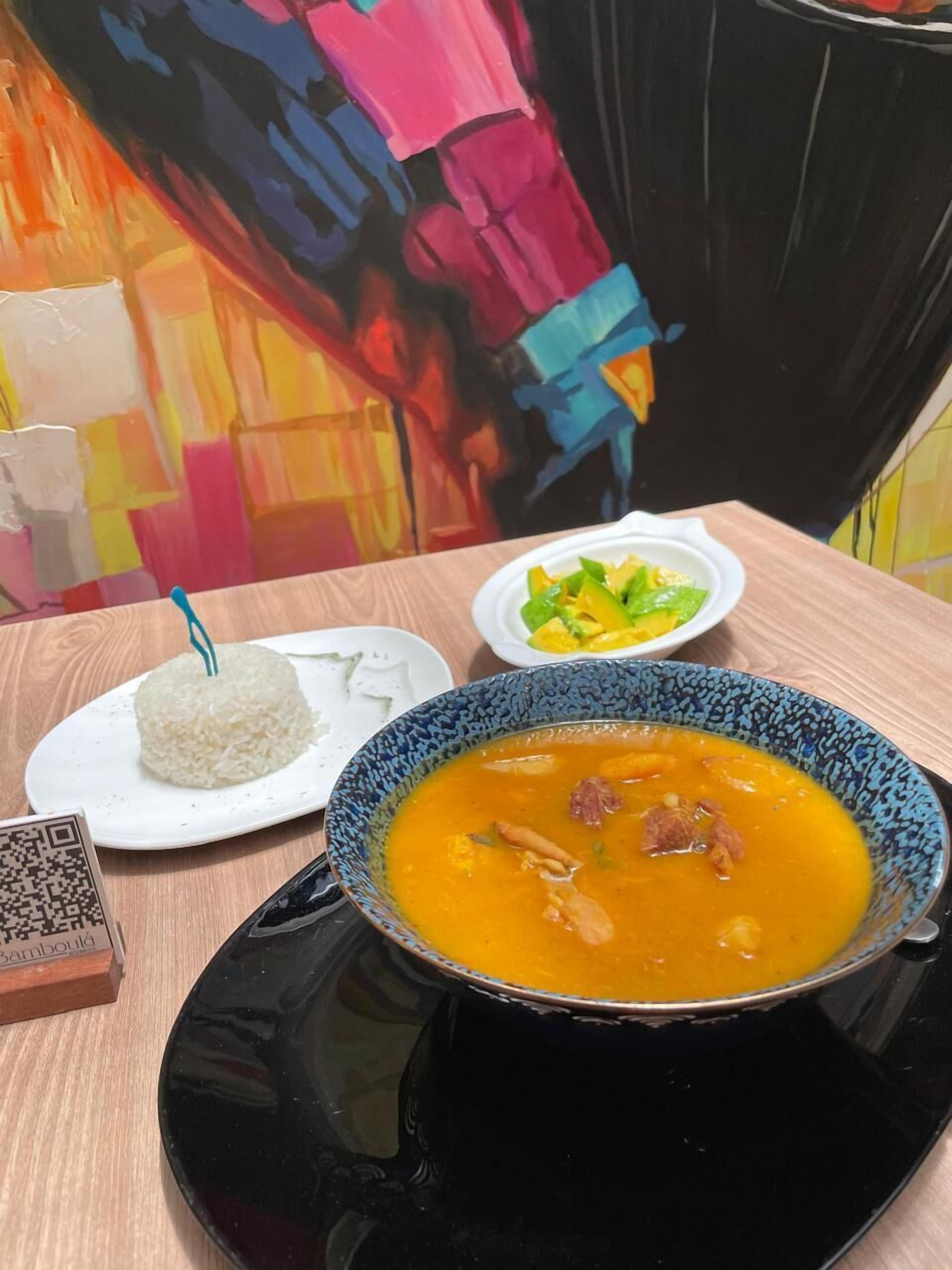 A table with a bowl of soup, a plate of rice, and a small dish of vegetables.