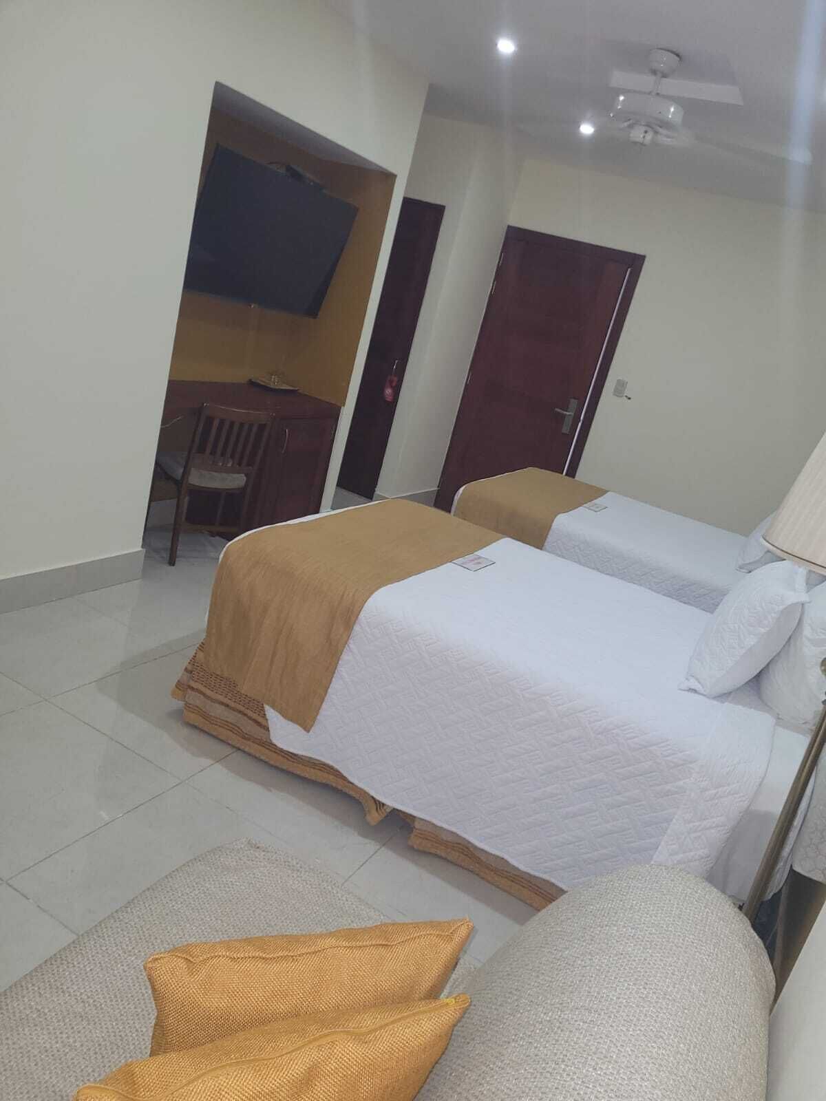 Una habitación de hotel con dos camas, un televisor montado en la pared y una puerta que da a otra habitación.
