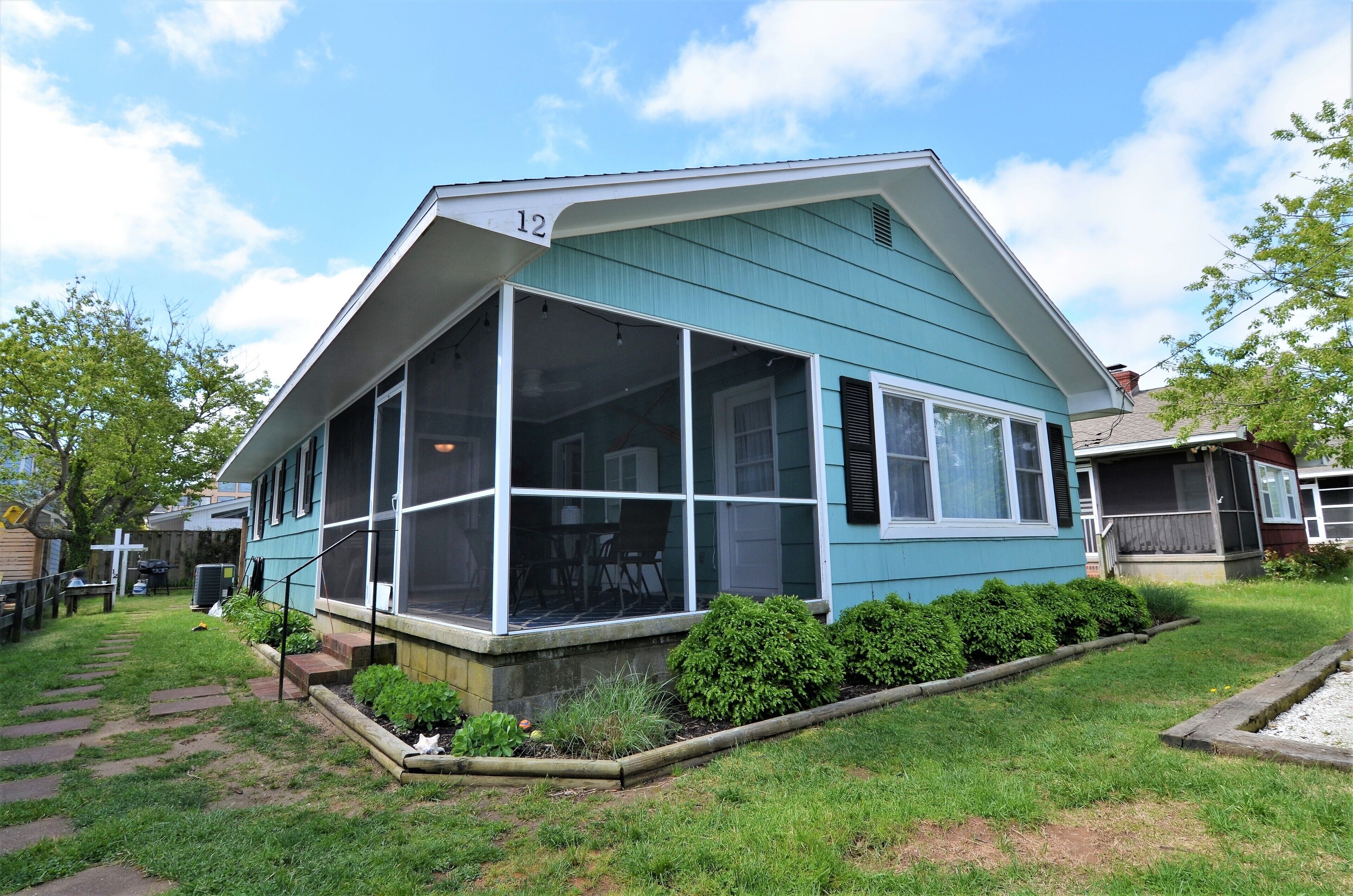 A blue house with a screened porch, number 12, and a well-maintained front yard.