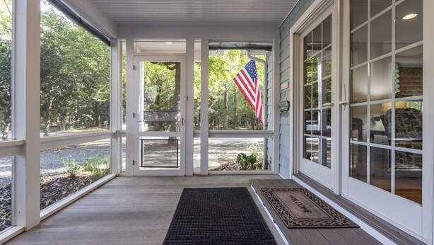 Eine überdachte Veranda mit Fußmatte, Blick ins Freie und eine amerikanische Flagge.