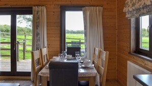 Une cabane en bois avec une table à manger dressée pour quatre personnes, deux chaises et une vue sur un paysage verdoyant par les fenêtres.