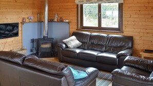 Un intérieur de chalet chaleureux avec une cheminée, des canapés en cuir et un téléviseur.