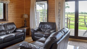 Un intérieur en bois avec des canapés en cuir, une lampe et une vue sur une terrasse en bois à l’extérieur.