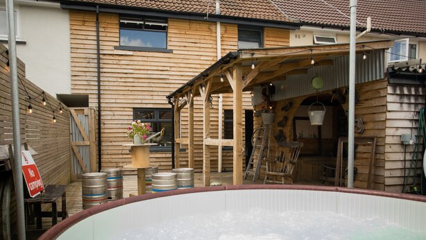 Eine Holzhütte mit Whirlpool, einer Holzterrasse und einem überdachten Sitzbereich im Freien.