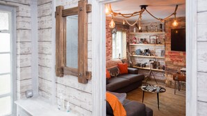 Ein rustikales Interieur mit freiliegenden Ziegelwänden, einem spiegelnden Holzbalken, einem grauen Sofa mit orangen Kissen und einem kleinen, runden Tisch.