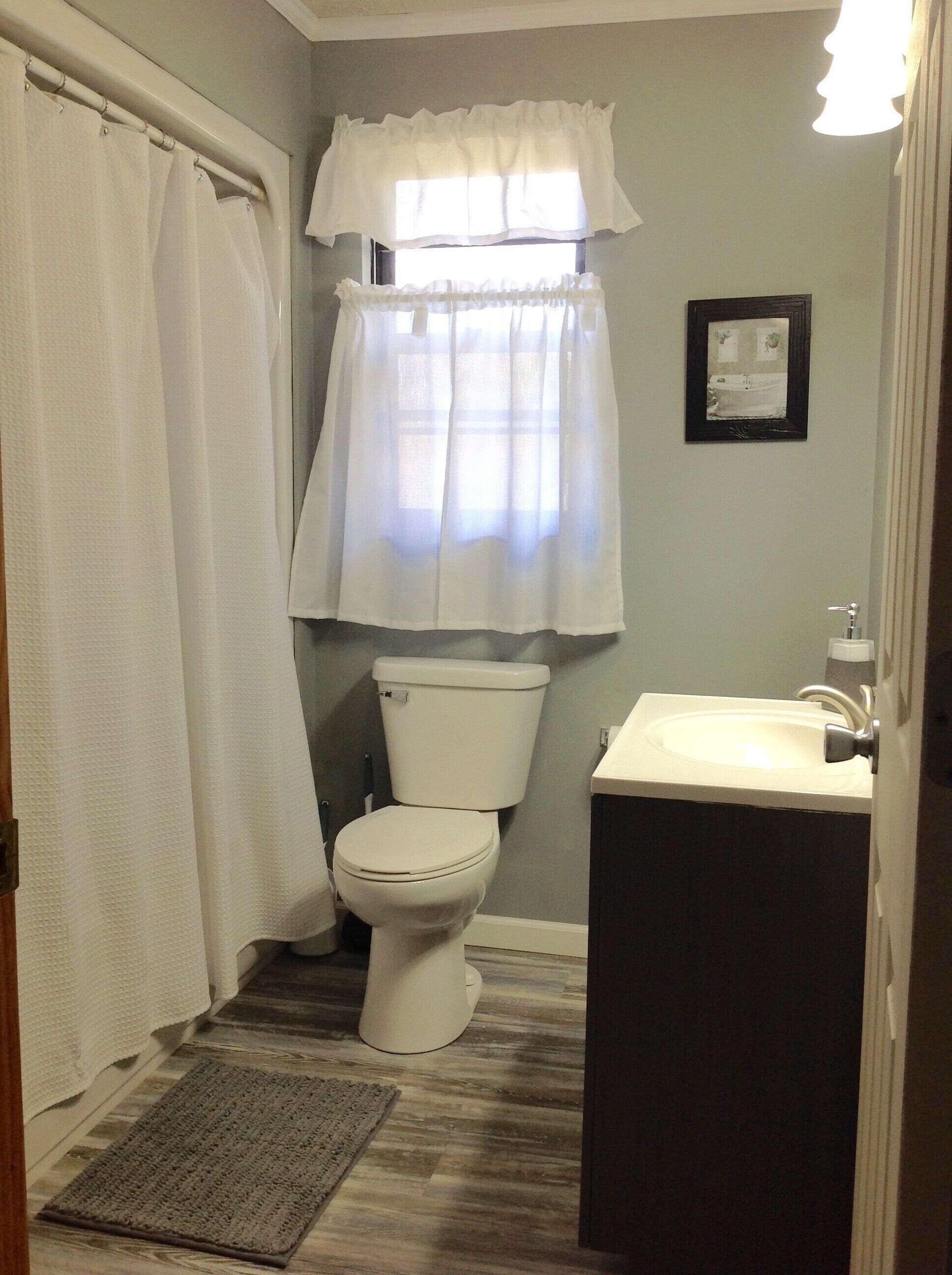 A bathroom with a toilet, sink, and window with a curtain.