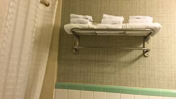 A bathroom with a towel rack holding three folded towels, a shower curtain, and a green-tiled wall.