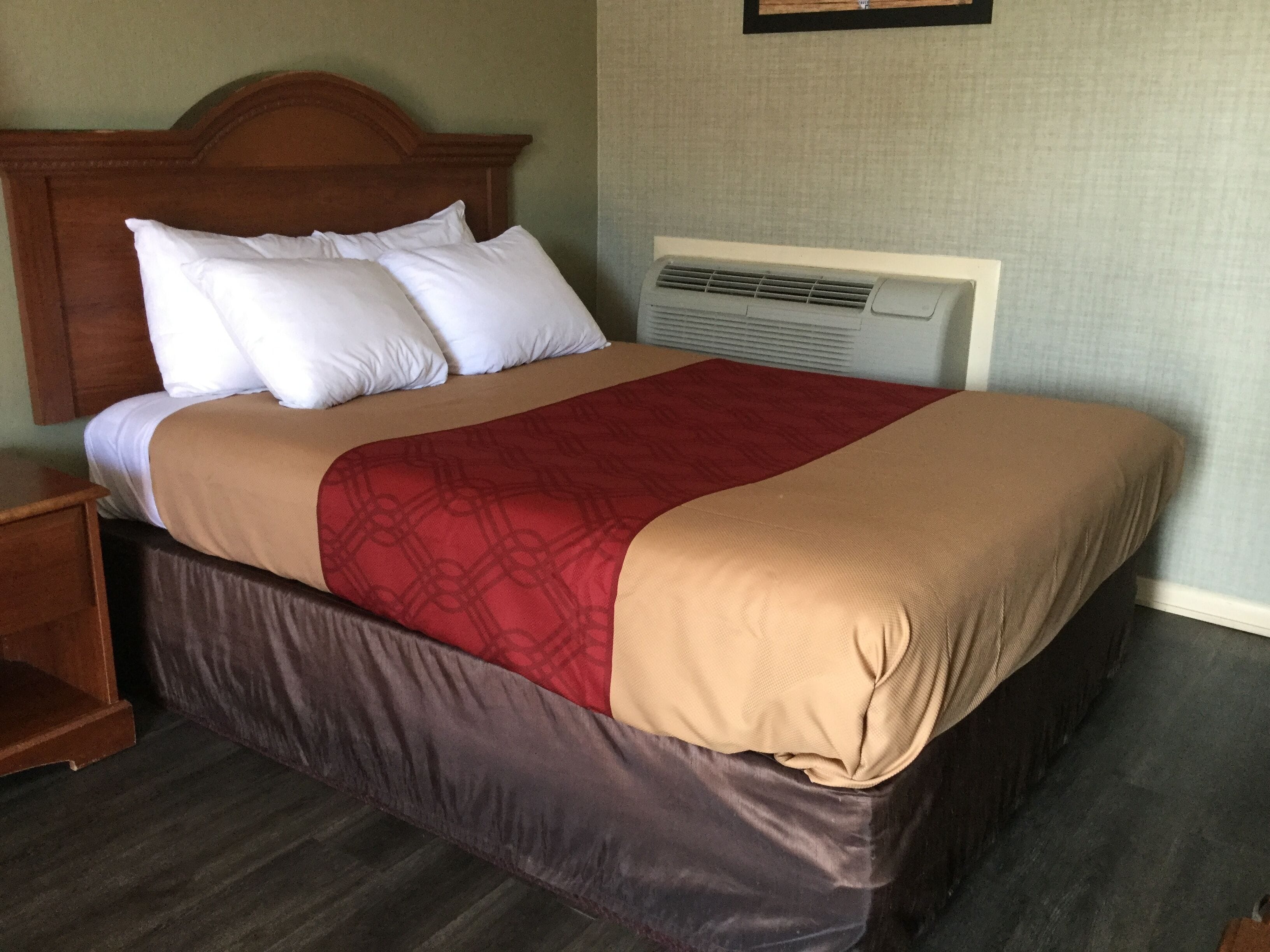 A neatly made bed with a wooden headboard, a red and beige bedspread, and white pillows.
